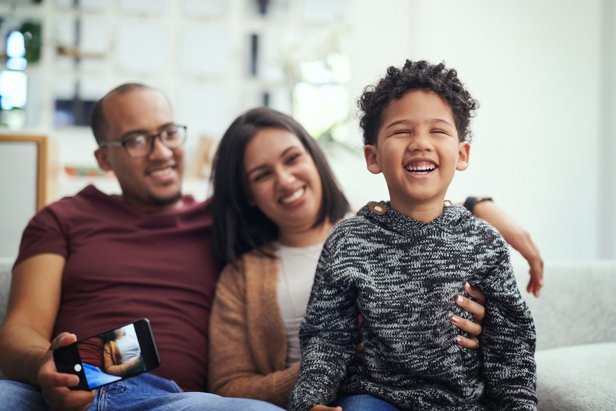 Shot of a young family sitting on the couch trying to take a photo with their son at home